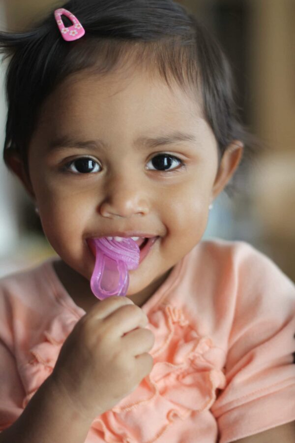 Baby with its first soft, silicone toothbrush and teether, pink